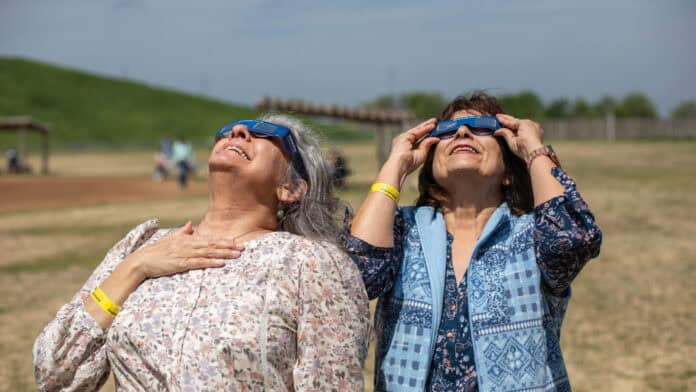 Two women watch the 2024 eclipse through their eclipse glasses.